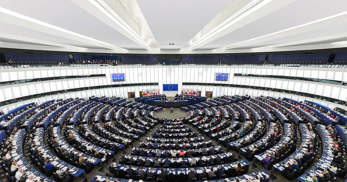 The European Parliament hemicycle chamber in session beneath the EU flag